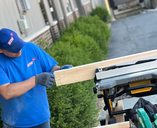 WowFix master in branded cap cutting replacement stock on the table saw at a job site