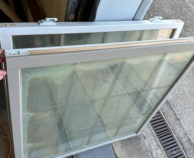 Old fogged insulated glass unit next to the new clear unit that replaces it — the $198 repair