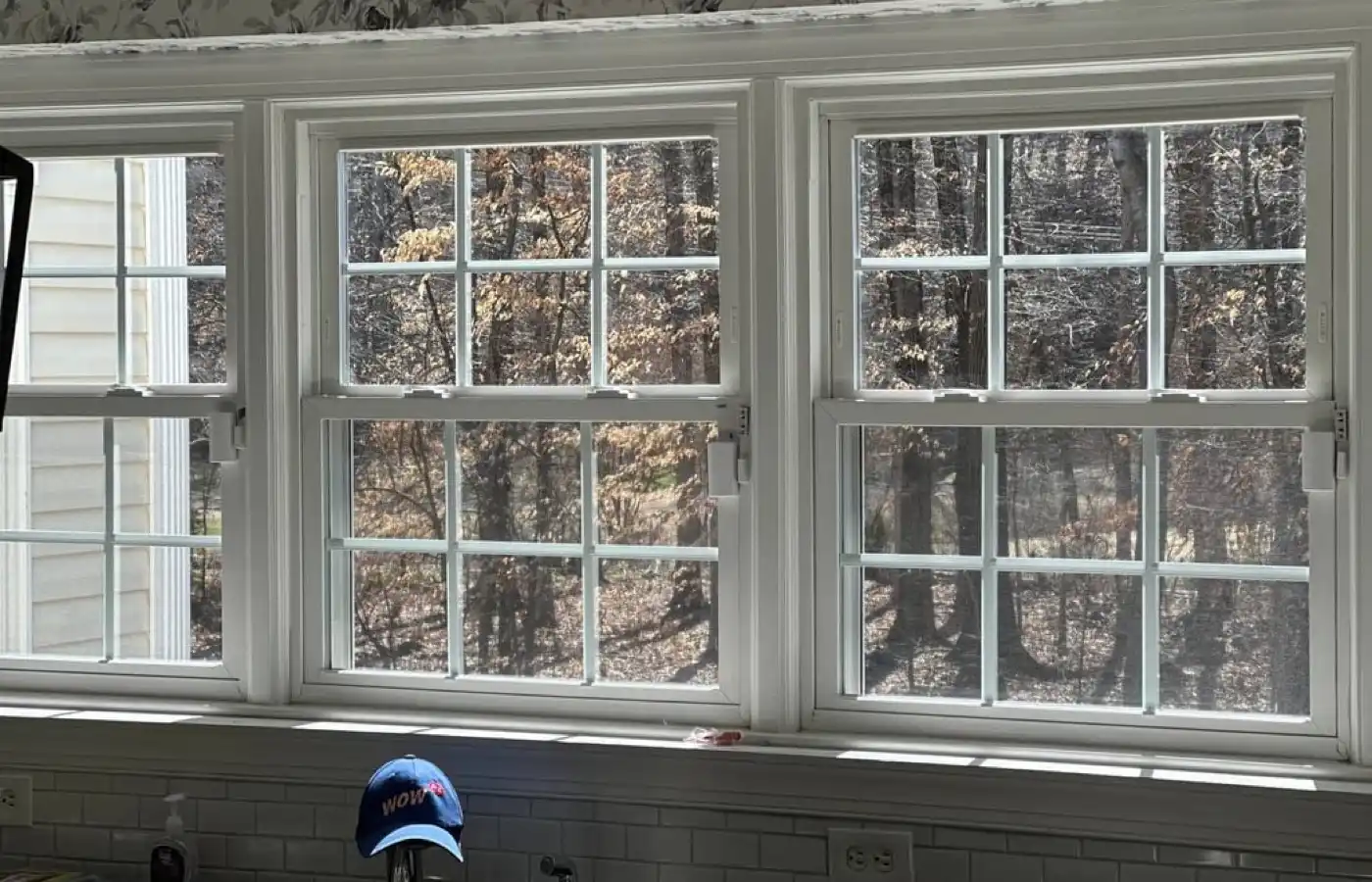 Three crisp double-hung grid windows over a kitchen sink after WowFix repair — WowFix cap on the faucet