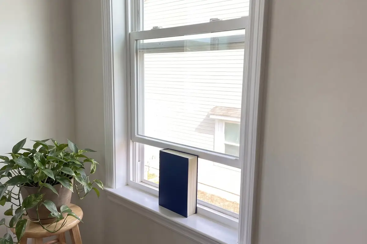 White vinyl double-hung window with the lower sash propped open by a book because it will not stay up