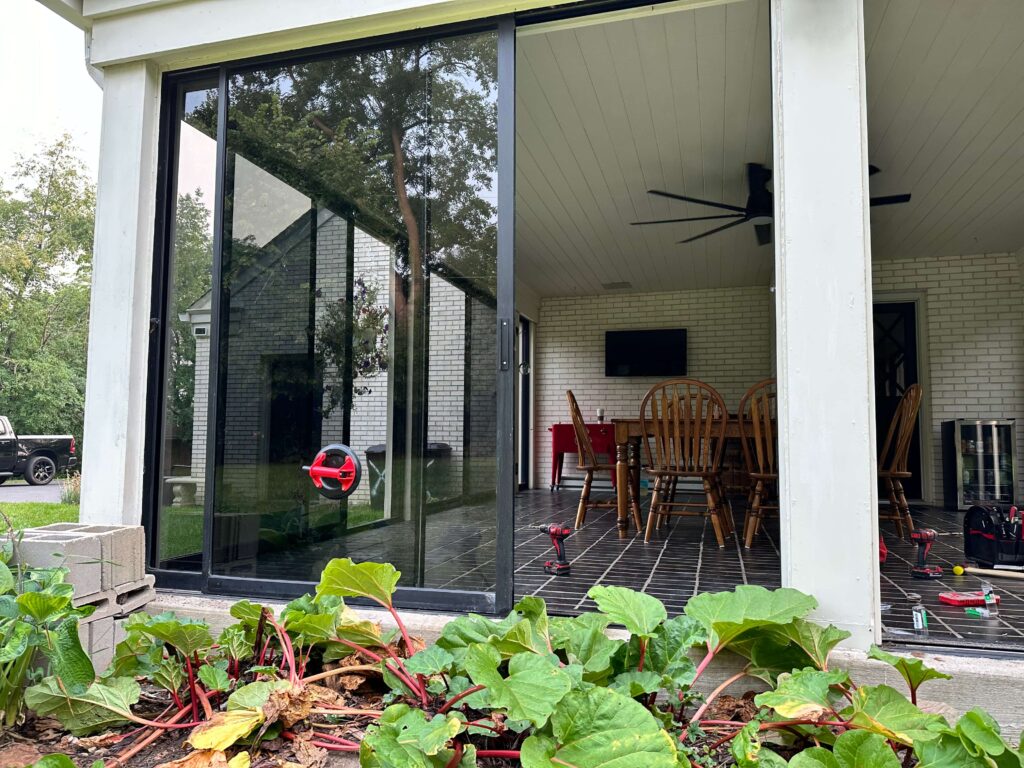 Large sliding glass patio door installation in modern brick home with interior dining room view and professional installation tools