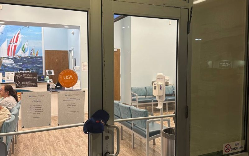 Commercial glass door entrance to medical office suite showing waiting room with blue chairs and professional certification displays