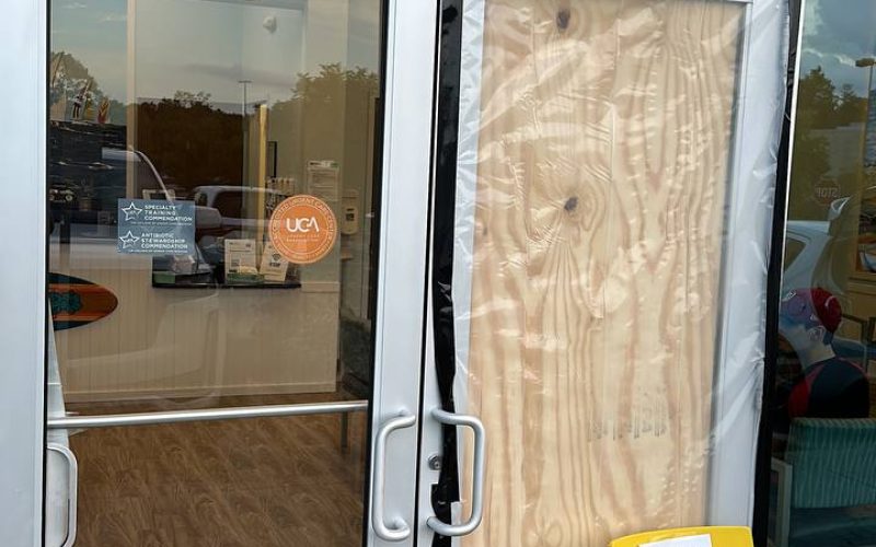 Commercial storefront with emergency board-up service showing contrast between damaged and intact glass doors with unit numbers
