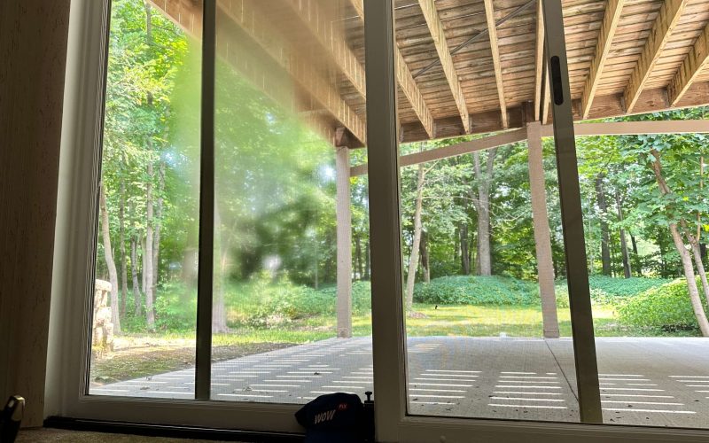 Modern sliding glass door installation overlooking forested backyard with covered porch, demonstrating professional window installation