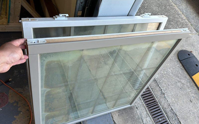 Foggy double-pane window repair in progress, showing condensation between glass panes and aluminum frame being serviced