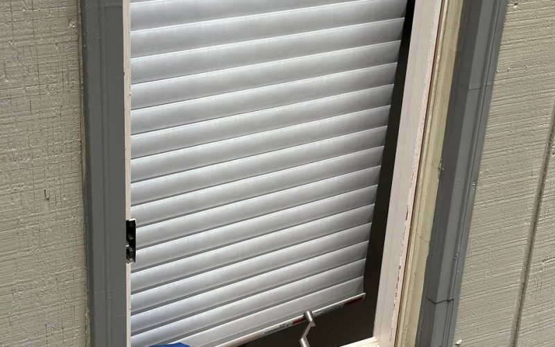 Damaged window sill with deteriorating wood frame and white horizontal blinds, showing need for professional window repair services