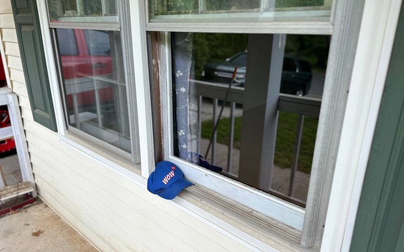 Worn window frame with WOW company hat showing deterioration and aging, demonstrating need for professional window replacement